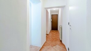 A narrow hallway with white walls and a tiled floor leading to a door. - GuestHost - In the heart of Genoa, on Via Rivoli, a cozy 60 sqm apartment ideal for 3 guests. Located on the -1 floor of a building without an elevator, it offers comfort and tranquility just steps from the lively city center. The area is well served by  (Genova)