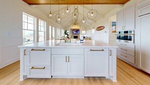 A spacious kitchen with a large island, white cabinetry, gold handles, and a wooden ceiling. - SBT115 Private Pool, Pickleball Court, Sauna, Boardwalk to the Beach (Port Aransas)