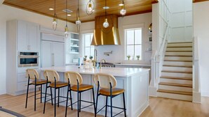 A modern kitchen with a central island, bar stools, and pendant lighting. - SBT115 Private Pool, Pickleball Court, Sauna, Boardwalk to the Beach (Port Aransas)