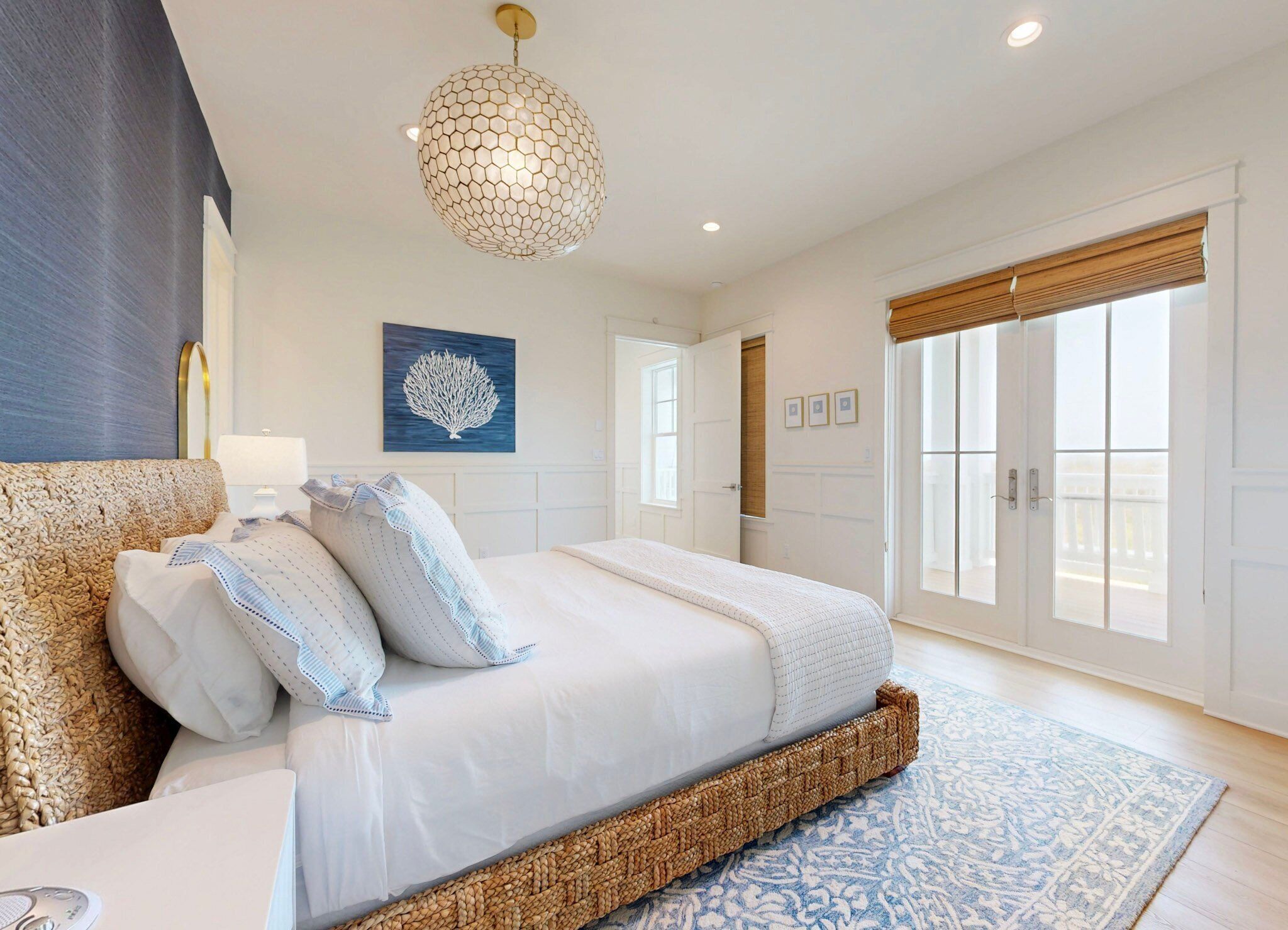 A bedroom with a large bed, a hanging light fixture, a wall art piece, and a view of the outside through a sliding door.