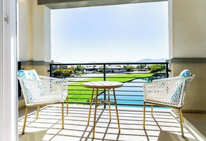 A balcony with two white wicker chairs, a small round table, and a view of a swimming pool and greenery. - Lakeside Living! WOW! Sleeps 10! 4 Primary Suites (Indio)