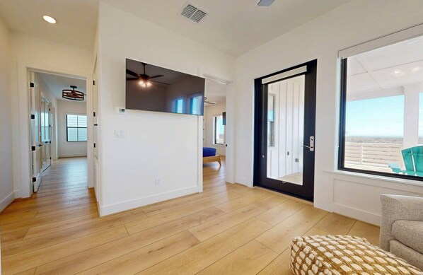 A spacious living area with a wooden floor, a black-framed door, and a view through a large window.