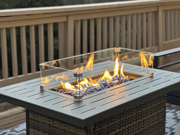 A rectangular outdoor fire feature with a clear glass enclosure, surrounded by a deck with wooden railings.
