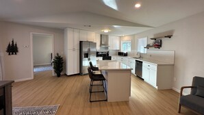 A modern kitchen with white cabinets, a stainless steel refrigerator, and a central island with bar stools.