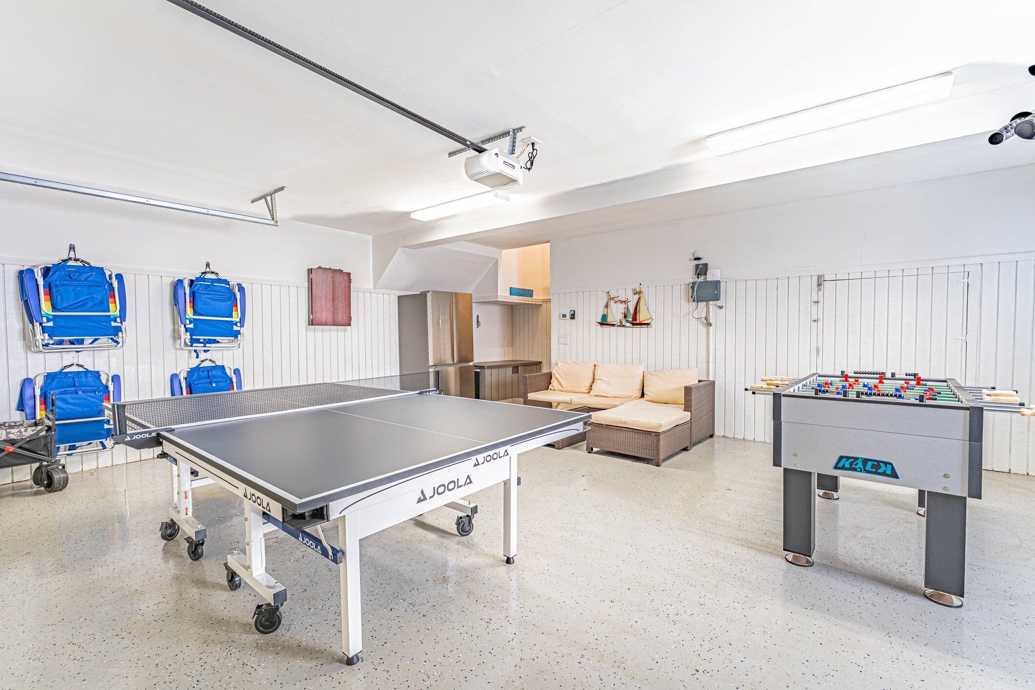 A room with a foosball table, a ping pong table, and a sofa.