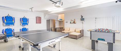 A room with a foosball table, a ping pong table, and a sofa.