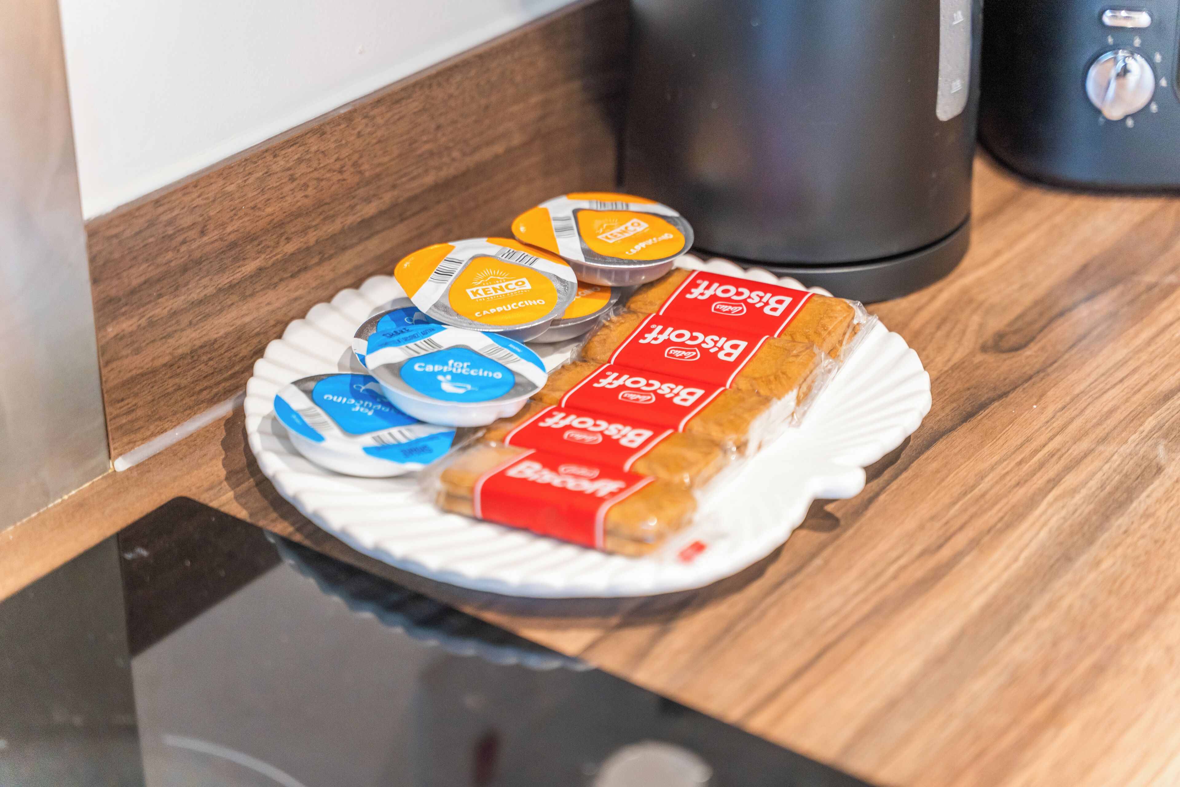 A plate with a sandwich and coffee pods on a wooden surface.