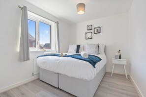 Quarto com cama grande, janela com cortinas, mesa de cabeceira e quadros na parede.