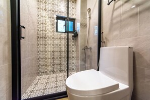 Un baño moderno con ducha de mampara de vidrio, un inodoro y baldosas con diseño.