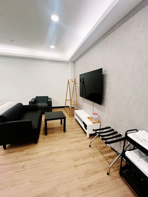 Quarto de hotel moderno com televisão de tela plana na parede, um sofá, uma pequena mesa e um banco.