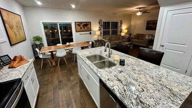 Una cocina moderna con encimeras de granito, lavavajillas integrado y un comedor con mesa y sillas de madera.