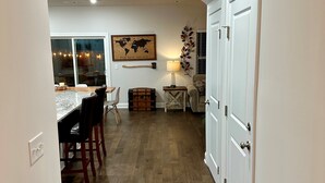 Una cocina con suelo de madera, paredes blancas y una zona de comedor con sillas y una mesa.