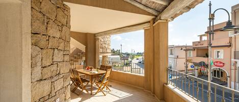 Un balcon avec un mur en pierre, une table et des chaises en bois, et une vue sur la rue et les immeubles.