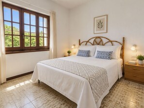A bedroom with a bed, a window with curtains, a wall-mounted plant, and a bedside table with a lamp. - Vacation home Itaca by Interhome (Villasimius)