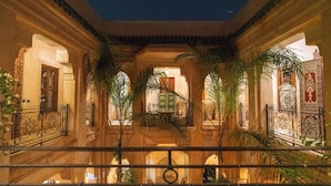 An indoor courtyard with arches, palm trees, and a balcony with wrought iron railings. - Palais Nejma (Marrakech)