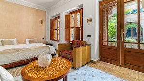 A bedroom with a bed, a small table, a sofa, and a large wooden door with glass panels. - Palais Nejma (Marrakech)