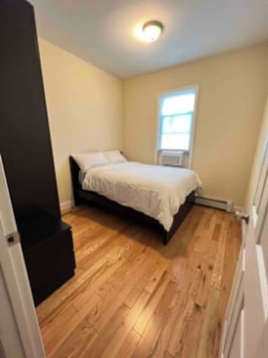 A bedroom with a bed, wooden flooring, a window, and a door. - Harrel Vacation Rentals (Omaha)
