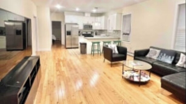 A spacious living area with a wooden floor, a black sofa, a round coffee table, and a kitchen in the background. - Harrel Vacation Rentals (Omaha)