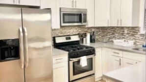 A modern kitchen with white cabinets, stainless steel appliances, and a wooden floor. - Harrel Vacation Rentals (Omaha)