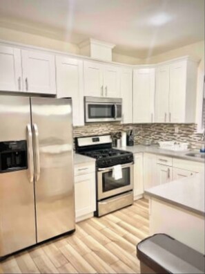 A modern kitchen with white cabinets, stainless steel appliances, and a wooden floor.