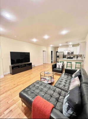 A living room with a black leather sofa, a coffee table, and a flat-screen TV.