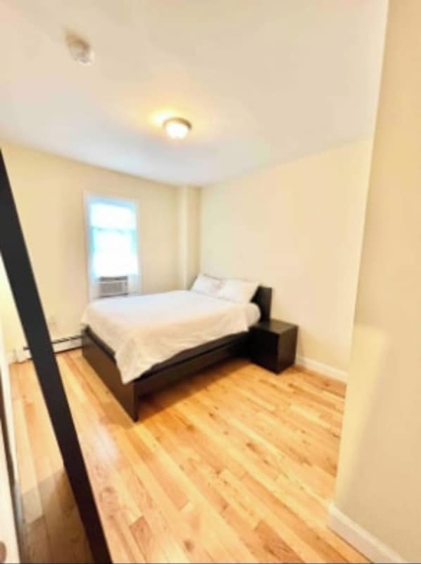 A bedroom with a bed, a nightstand, and a window. - Harrel Vacation Rentals (Omaha)
