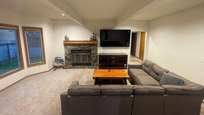 Ein Wohnzimmer mit Kamin aus Stein, einem an der Wand befestigten Flachbildfernseher, einem grauen Sofa und einem Holztisch.