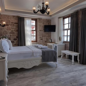 A bedroom with a stone wall, a bed, a TV, and a bench. - Cunda Taka (Ayvalik)