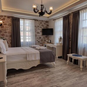 A bedroom with a stone wall, a bed, a desk, a television, and a chandelier. - Cunda Taka (Ayvalik)