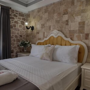 A hotel room with a stone wall, a bed with white bedding, a nightstand with a lamp, and a window with curtains. - Cunda Taka (Ayvalik)
