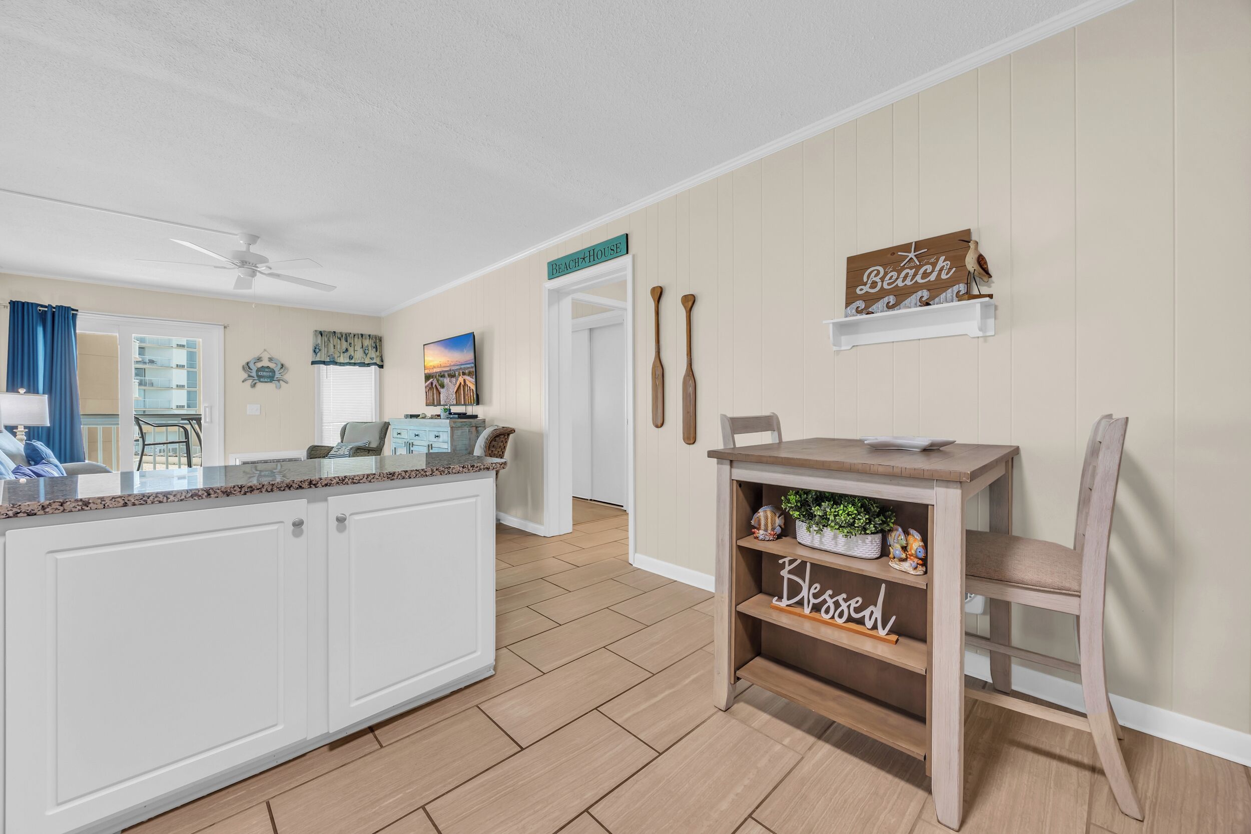 A kitchen with a wooden table, a chair, and a shelf with decorative items.