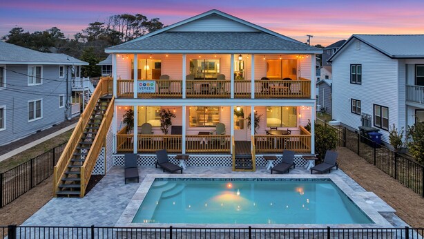 Ein zweistöckiges Haus mit Pool, einer Holzterrasse und Sitzgelegenheiten im Freien.