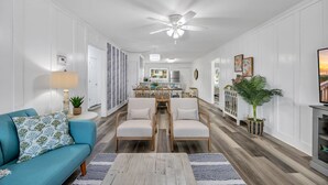 Ein geräumiges Wohnzimmer mit einem blauen Sofa, zwei Sesseln, einem Couchtisch und einem Essbereich im Hintergrund.