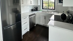 Una cocina moderna con armarios blancos, electrodomésticos de acero inoxidable y un amplio ventanal con vistas al exterior.