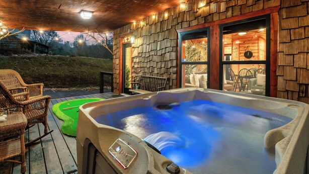 A hot tub on a wooden deck with wicker chairs, a wooden wall, and a view of the outdoors.