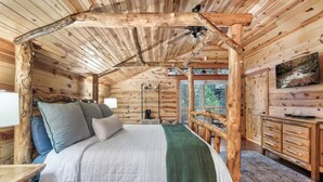 A wooden cabin bedroom with a four-poster bed, a green throw blanket, and a wooden dresser.