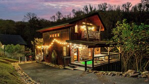 A two-story wooden cabin with a porch, a stone pathway leading to the entrance, and a small deck with chairs.