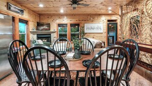 A wooden interior with a dining table, chairs, a ceiling fan, and a fireplace.