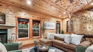 A cozy living room with a wooden ceiling, a fireplace, a sectional sofa, and a coffee table.