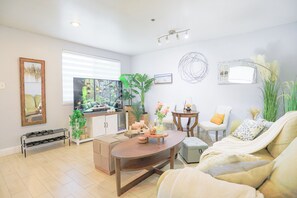A modern living room with a sofa, coffee table, and a dining area with a bench. There are plants, a TV, and a window with blinds. - Sunnyvale 3B2b Super Big House (Sunnyvale)