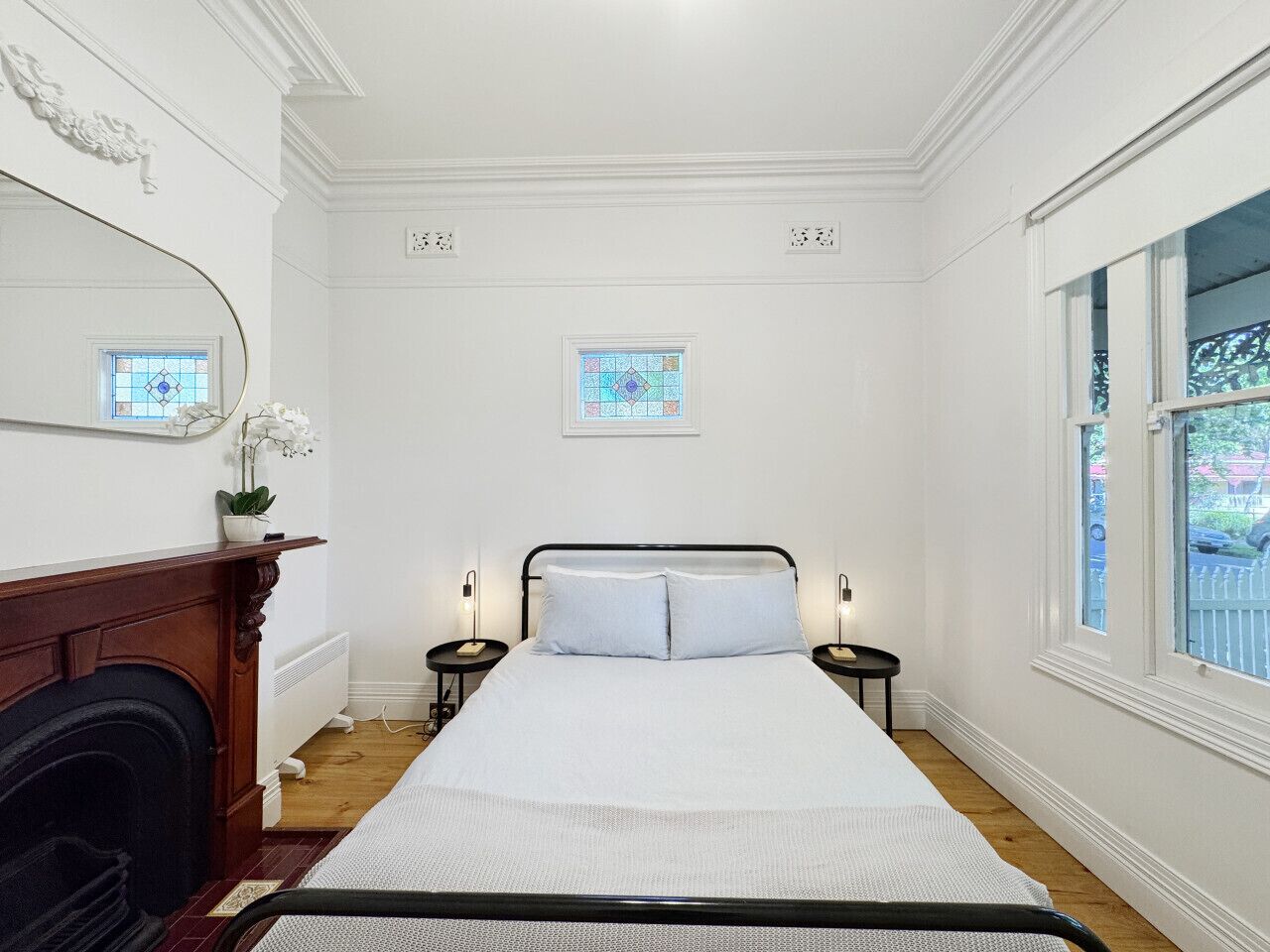 A bedroom with a large bed, two bedside tables, a fireplace, and two windows with stained glass.