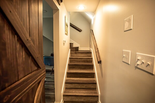 A wooden staircase with a handrail, a light switch, and a power outlet on the wall.