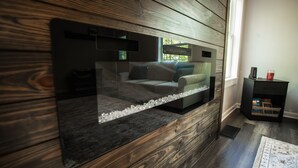 Ein modernes Wohnzimmer mit einem großen Flachbildfernseher an einer Holzwand, einem grauen Sofa mit blauen Kissen und einem kleinen schwarzen Beistelltisch mit einem roten Gegenstand darauf.