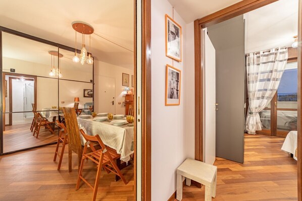 A dining area with a table set for four, wooden chairs, a bench, and a view through a glass door.