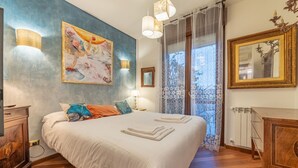 A bedroom with a large bed, a painting on the wall, a wooden dresser, and a window with curtains. - 5' from Bocconi University with 2 Bedr and 2 Bathr (Milano)