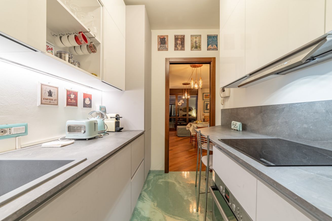 A narrow kitchen with a countertop, a toaster, and a sink. There is a wooden dining area in the background.