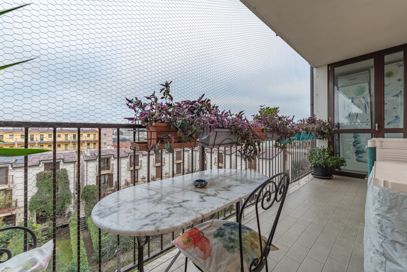 Un balcón con una mesa de mármol, plantas en macetas y vistas a edificios.