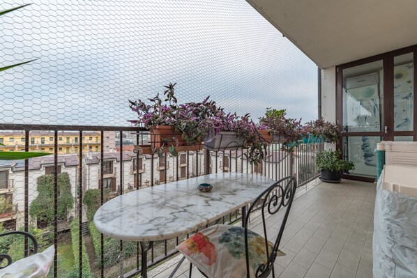 Un balcon avec une table en marbre, des plantes en pot et une vue sur les bâtiments.