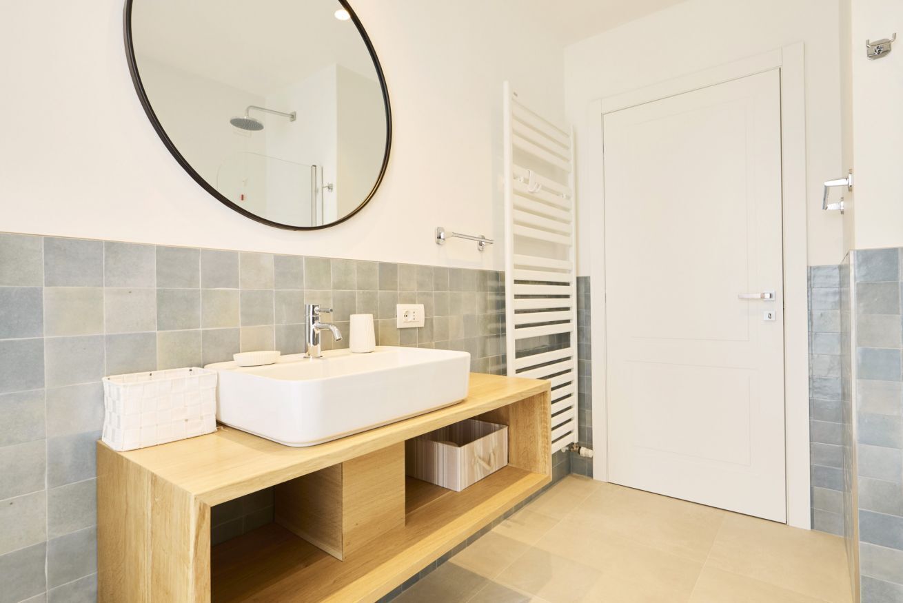 A modern bathroom with a large mirror, a white sink, and a towel rack.