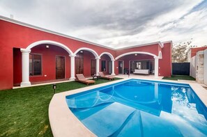 A red building with a swimming pool and outdoor seating.
